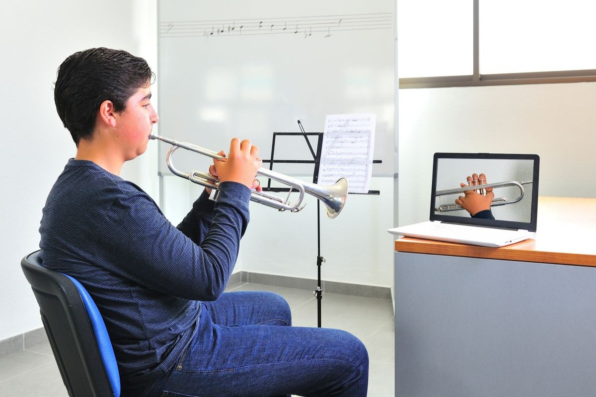 A teen with his laptop during a zoom call taking an online trumpet lesson